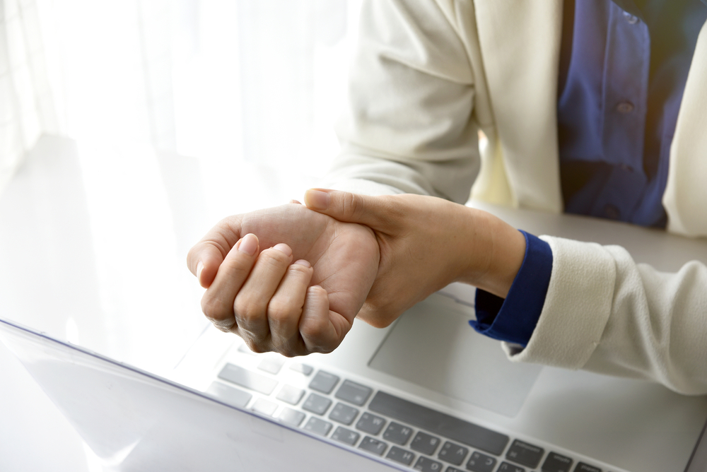 Femme assise devant son ordinateur qui et se tient le poignet qui semble faire mal